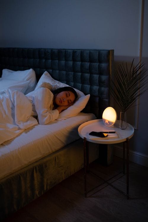 A woman sleeping peacefully on a bed in a dimly lit modern bedroom with soft ambient lighting