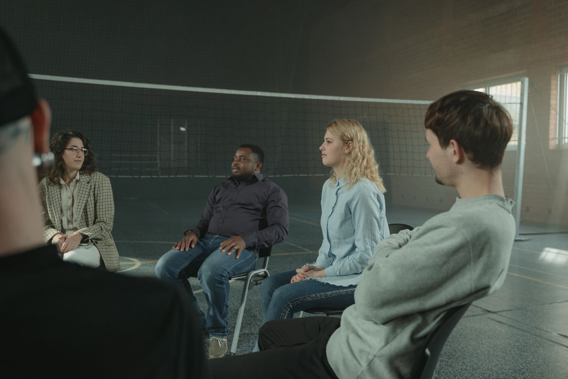 Diverse group of adults sitting in a circle during a supportive group therapy meeting